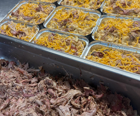 Cheese-topped pans beside a tray of pulled pork